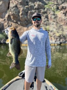 Justin Loflin holds a massive Largemouth with the rocky shoreline behind him during a guided fishing trip at Saguaro Lake