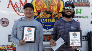 Bobby and Mason holding their first place trophies and check in front of the FishIn48 tournament trailer