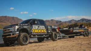 Lifted Truck with bass boat behind it next to the lake. Wrapped with Lifted Trucks branding